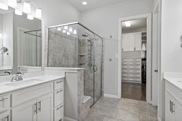 full bath with two vanities, a spacious closet, a sink, a shower stall, and tile patterned flooring