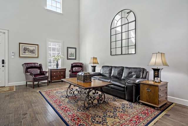 living area with a wealth of natural light, a towering ceiling, baseboards, and wood finished floors