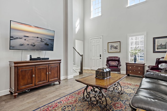 living room with light wood-style floors, a high ceiling, stairway, and baseboards