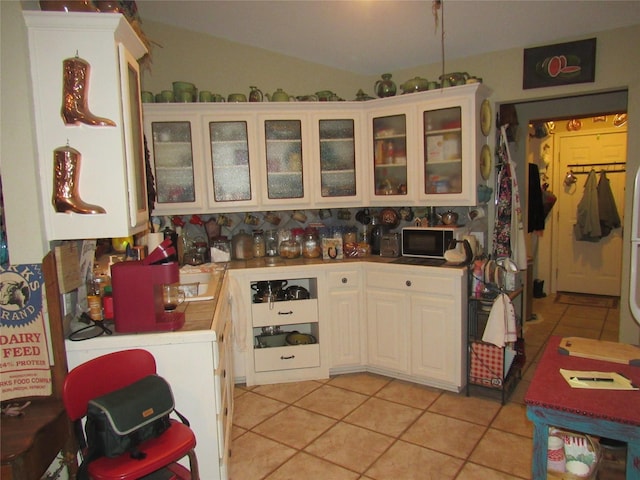 kitchen with white cabinets, light tile patterned floors, black microwave, and vaulted ceiling