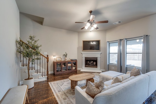 living area with a fireplace with raised hearth, ceiling fan, visible vents, baseboards, and stairs