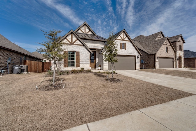 tudor home featuring brick siding, a standing seam roof, fence, a garage, and driveway