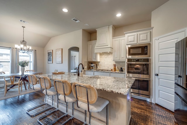 kitchen featuring stainless steel appliances, custom exhaust hood, a sink, and a center island with sink