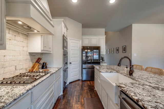 kitchen featuring stainless steel appliances, white cabinetry, a sink, light stone countertops, and premium range hood