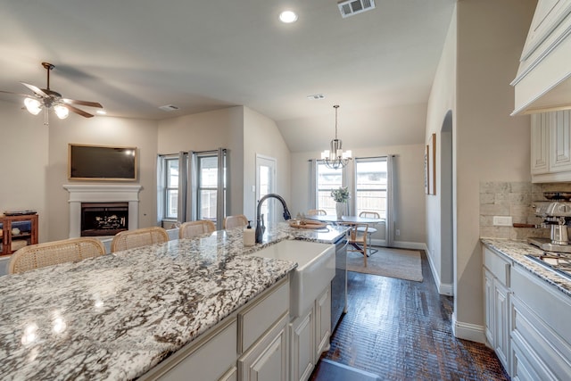 kitchen with visible vents, light stone counters, hanging light fixtures, a fireplace, and a sink