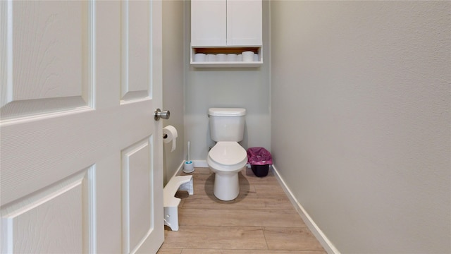 bathroom with toilet, baseboards, and wood finished floors