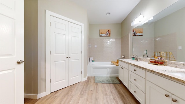 full bathroom with double vanity, a closet, a bath, wood finished floors, and a sink