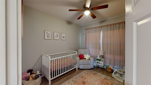 bedroom with ceiling fan, a crib, and wood finished floors