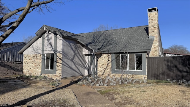 exterior space with a shingled roof, brick siding, fence, and a chimney