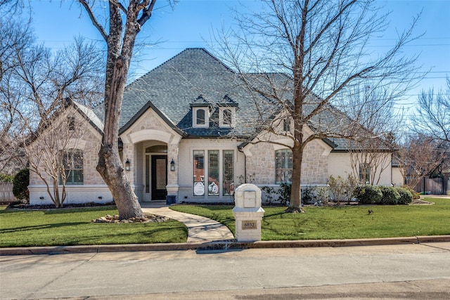 french provincial home featuring stone siding, brick siding, roof with shingles, and a front yard