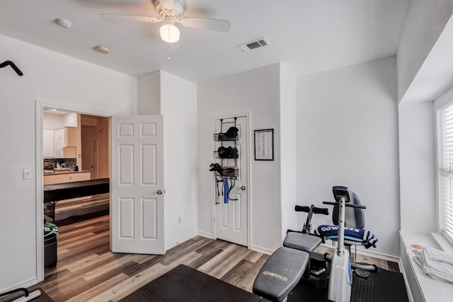 workout area with ceiling fan, light wood-type flooring, visible vents, and baseboards