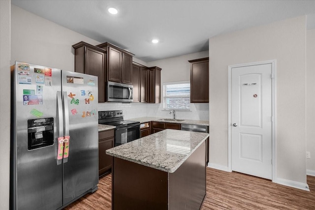 kitchen with appliances with stainless steel finishes, dark brown cabinetry, a kitchen island, a sink, and wood finished floors