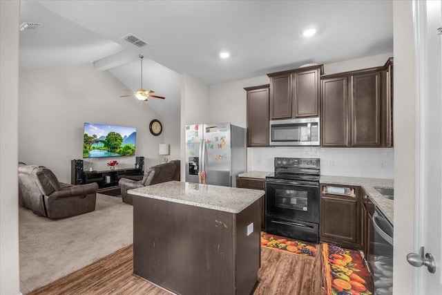 kitchen featuring visible vents, a kitchen island, appliances with stainless steel finishes, open floor plan, and light stone countertops