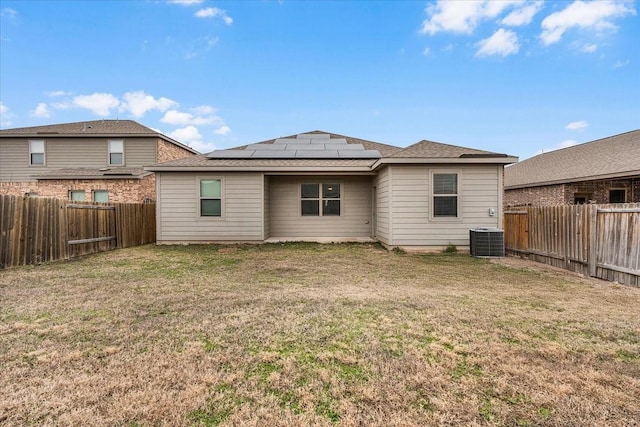 rear view of property with solar panels, a yard, cooling unit, and a fenced backyard