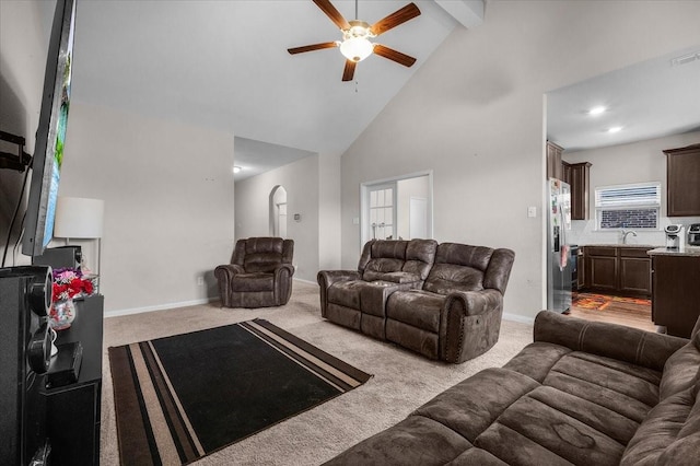 living room with baseboards, a ceiling fan, light colored carpet, beamed ceiling, and high vaulted ceiling