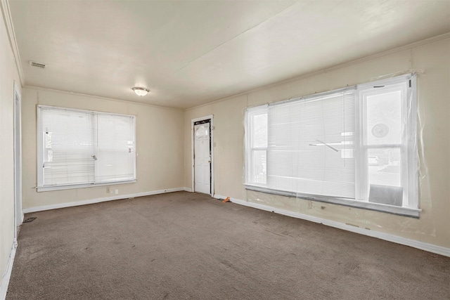 spare room with dark colored carpet, ornamental molding, visible vents, and baseboards