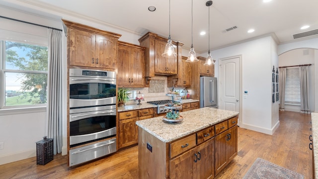 kitchen featuring stainless steel appliances, a center island, a warming drawer, brown cabinetry, and decorative light fixtures