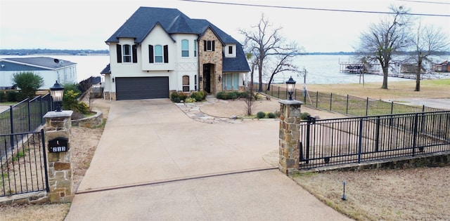 french country style house with a fenced front yard, concrete driveway, a water view, and stucco siding