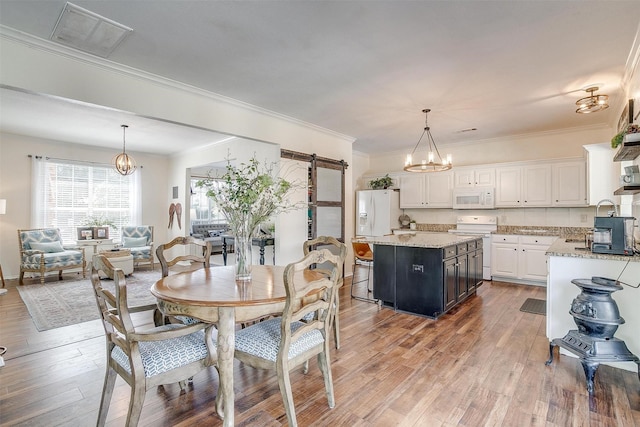 dining space with a barn door, light wood-type flooring, visible vents, and a notable chandelier