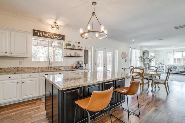 kitchen with visible vents, a center island, a sink, white cabinetry, and a notable chandelier