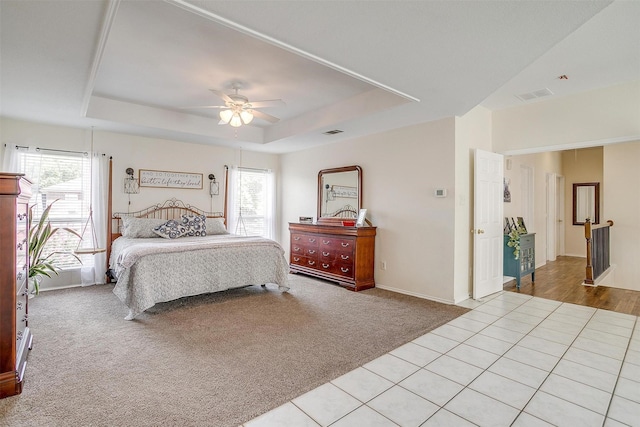 bedroom with light carpet, a tray ceiling, multiple windows, and visible vents