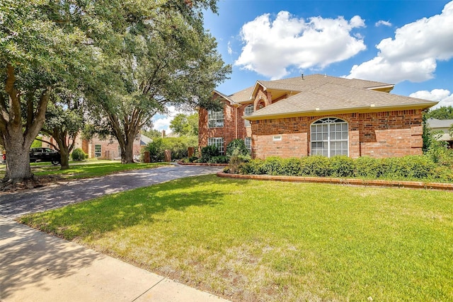 view of front of property featuring a front lawn, roof with shingles, and brick siding