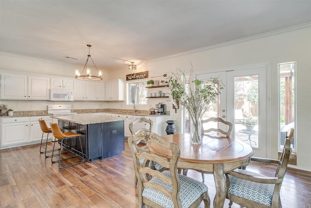 dining space featuring visible vents, light wood-style flooring, ornamental molding, an inviting chandelier, and french doors