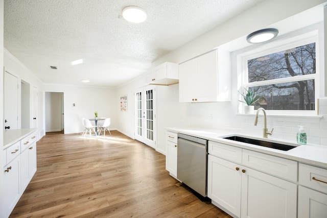 kitchen with a sink, white cabinets, light countertops, and stainless steel dishwasher