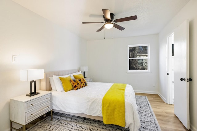 bedroom with a textured ceiling, light wood-type flooring, a ceiling fan, and baseboards