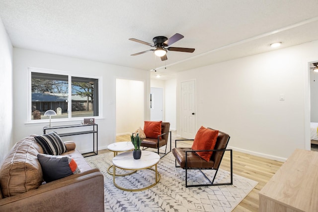 living room with light wood finished floors, ceiling fan, baseboards, and a textured ceiling