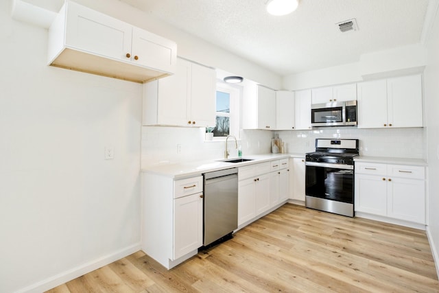 kitchen featuring light countertops, light wood-style flooring, appliances with stainless steel finishes, white cabinets, and a sink