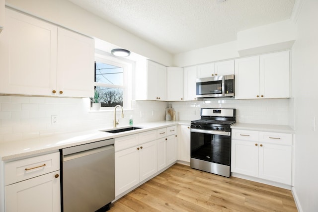 kitchen featuring stainless steel appliances, a sink, white cabinetry, light wood-style floors, and tasteful backsplash