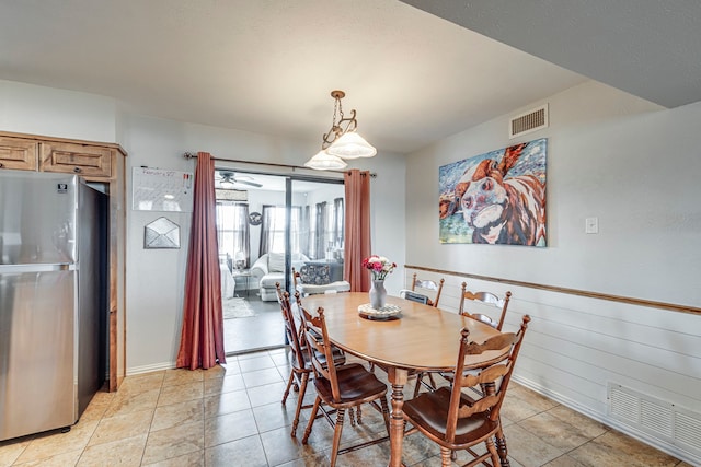 dining area featuring light tile patterned floors, wooden walls, visible vents, and wainscoting