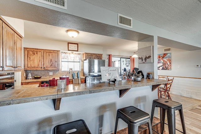 kitchen featuring a breakfast bar, freestanding refrigerator, visible vents, and a wainscoted wall