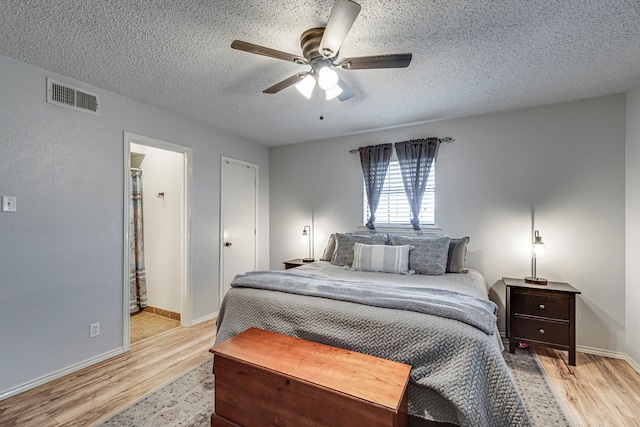 bedroom featuring light wood finished floors, baseboards, visible vents, and a textured ceiling