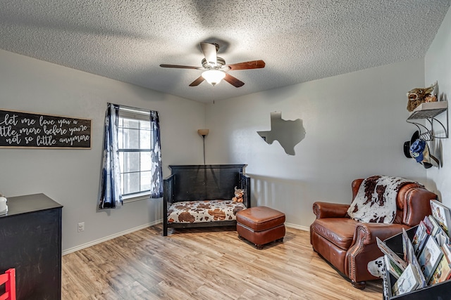 living area with light wood finished floors, a textured ceiling, baseboards, and a ceiling fan