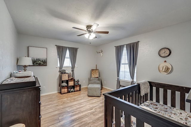 bedroom with ceiling fan, light wood finished floors, a crib, and baseboards