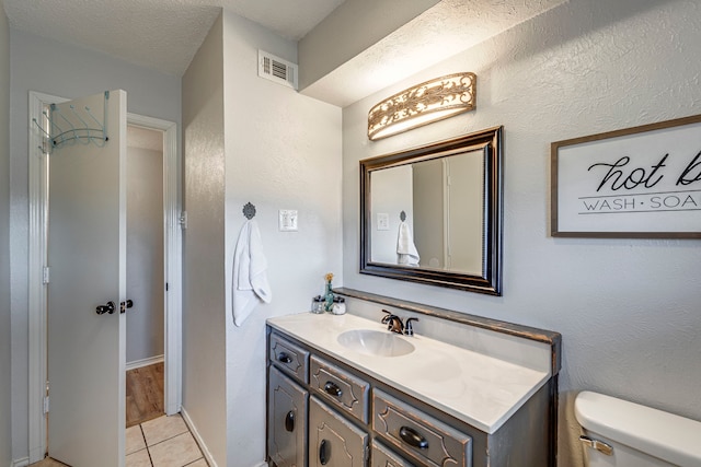 bathroom featuring a textured ceiling, toilet, vanity, visible vents, and tile patterned floors