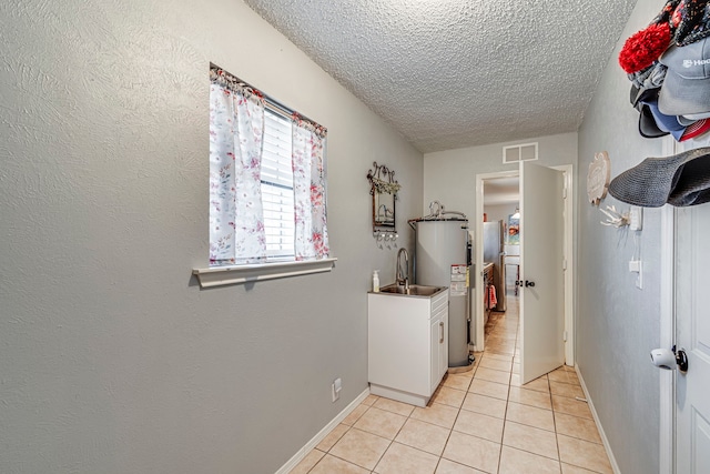 washroom featuring a textured ceiling, light tile patterned flooring, a sink, visible vents, and baseboards