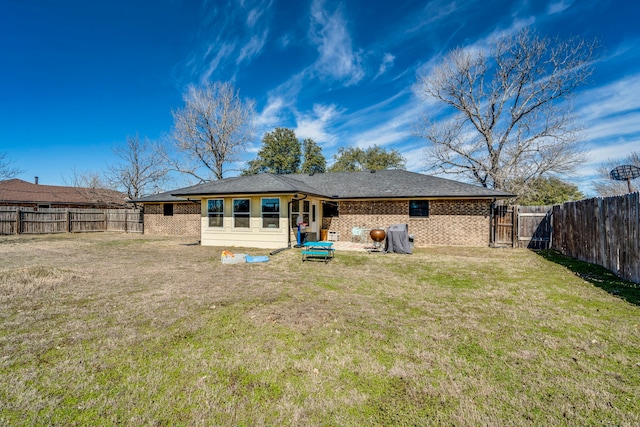 rear view of property featuring a fenced backyard, a lawn, and brick siding