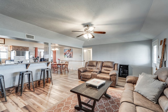 living room featuring a textured ceiling, light wood finished floors, visible vents, and a ceiling fan