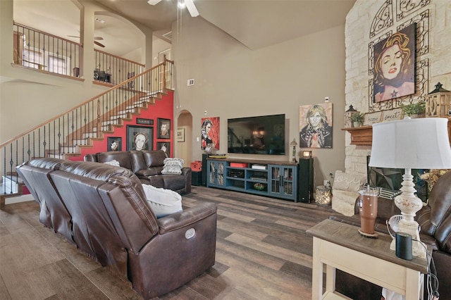 living room featuring arched walkways, ceiling fan, wood finished floors, stairs, and a fireplace