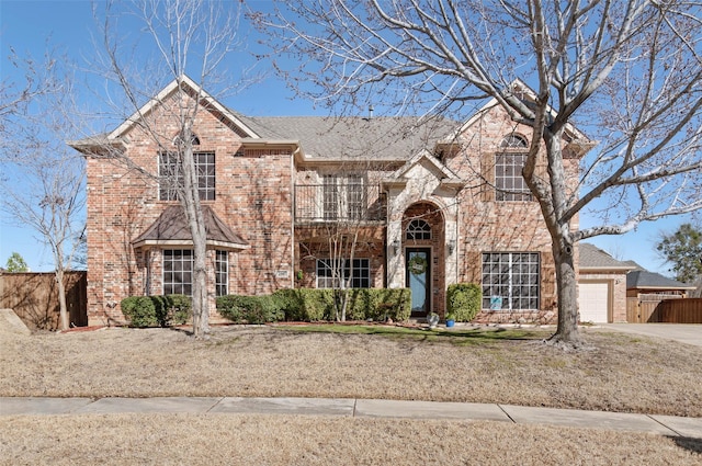 traditional-style house featuring a garage, brick siding, fence, concrete driveway, and a front yard