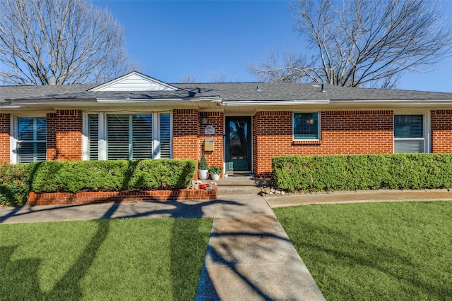 view of front of home featuring a front yard, brick siding, and roof with shingles