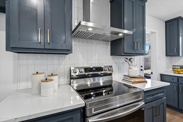 kitchen with electric range, tasteful backsplash, light stone countertops, blue cabinetry, and wall chimney range hood