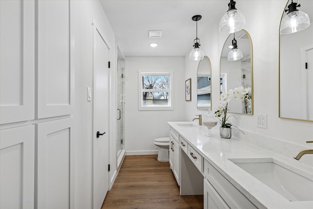 full bathroom with double vanity, toilet, wood finished floors, a shower stall, and a sink