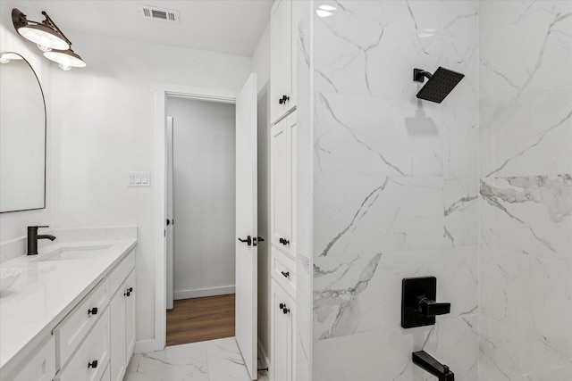 bathroom with marble finish floor, a marble finish shower, visible vents, vanity, and baseboards