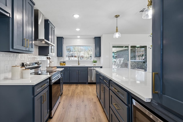 kitchen featuring visible vents, wall chimney exhaust hood, stainless steel appliances, light wood-type flooring, and a sink