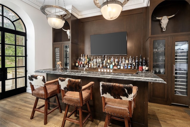 bar with a dry bar, light wood-style flooring, a high ceiling, and crown molding