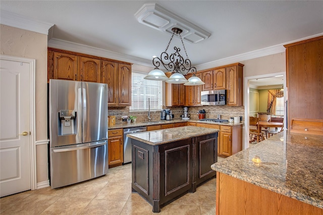 kitchen featuring a center island, pendant lighting, crown molding, stainless steel appliances, and light stone countertops